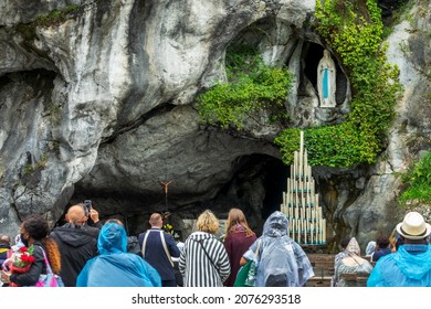 LOURDES, FRANCE - AUGUST 16, 2021: Pilgrims praying the statue of Virgin Mary in the grotto of Our Lady of Lourdes, France