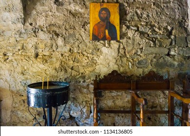 Lousios, Greece/ June, 2018: Religious Scene With An Icon Of Jesus, A Votive Stand With A Candle And Traditional Wooden Seats Inside An Old Monastery Near Lousios Gorge In Arcadia Greece