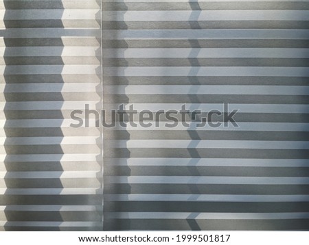 Louvered curtain with zigzag pattern shadow. Pleated louvers or blinds. Abstract interior background. Closeup of modern architecture detail. Polygonal geometric structure of parallel lines and stripes