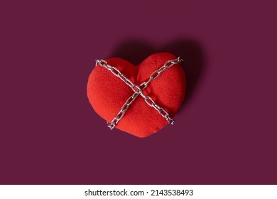 Love addiction. A toy heart rewound by a chain on a colored background. Space for text - Shutterstock ID 2143538493