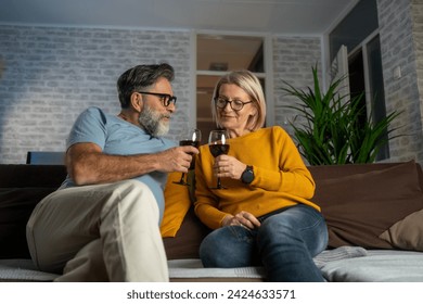 Love is in the air. Beautiful mature couple drinking wine while sitting on the sofa at home. Two senior adults at home - Beautiful couple relaxing and watching a movie at tv - Powered by Shutterstock