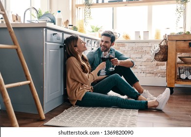 Love is in the air. Beautiful young couple drinking wine while sitting on the kitchen floor at home - Shutterstock ID 1369820090