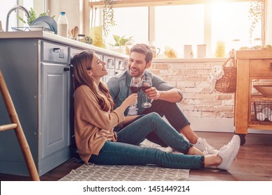 Love is in the air. Beautiful young couple drinking wine while sitting on the kitchen floor at home
