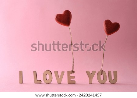 Love background with cutouts of letters forming the phrase i love you and two red heart-shaped glitter balloons held by a jute thread flying. Front view.