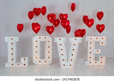 Love big letters with led retro bulbs glowing. Word LOVE illuminated with a big letters. Inscription is love. Glowing large letters. Wedding decor. Red heart balloons. air balls in shape of red heart
