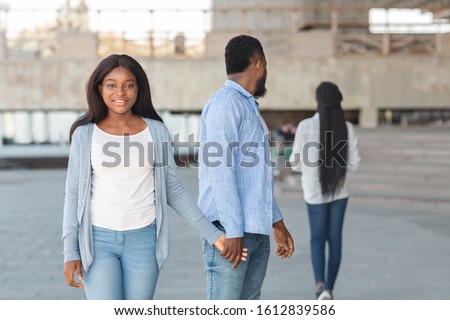 Love is blind. Unfaithful black guy turning head and staring at another woman while walking with his unsuspectful girlfriend, selective focus