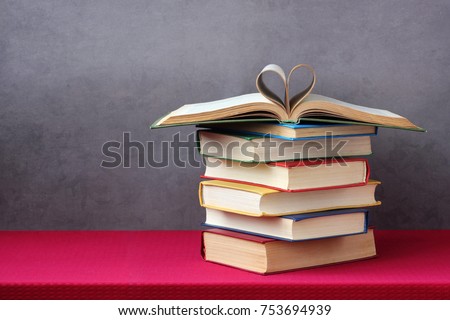 Love of books, reading. Stack of books in the colored cover lay on the table. Open book with curled leaves in the shape of a heart. Library, education.  Empty space for Your text on the left.