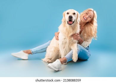 Love And Care Concept. Cheerful young lady patting her happy labrador spending time together, embracing pet, posing looking at camera sitting on the floor isolated on blue background, full body length