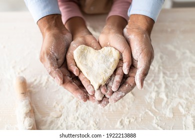 Love And Care Concept. Closeup above top view of unrecognizable african american man and girl baking cake in the kitchen and holding dough in heart shape in hands, dad and daughter cooking together - Shutterstock ID 1922213888