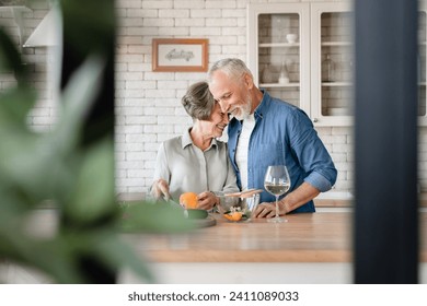 Love and care concept. Quality time and acts of service - love language. Senior old couple grandparents hugging cuddling helping prepare food cook romantic dinner and drinking wine at home kitchen - Powered by Shutterstock