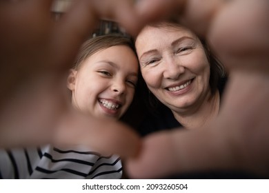 With Love And Care. Smiling Old Age Granny Tween Girl Grandkid Look At Camera Through Tender Heart Of Joined Fingers. Aged Woman Custodian Shoot Affectionate Selfie Portrait With Preteen Foster Child