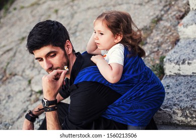 Love Caring Relations Between Father And Daughter, Young Man Wear Baby Toddler Girl In Blue Sling Wrap Carrier Scarf Back And Give Her Small Daisy Flower Outdoors, Baby Wearing Concept