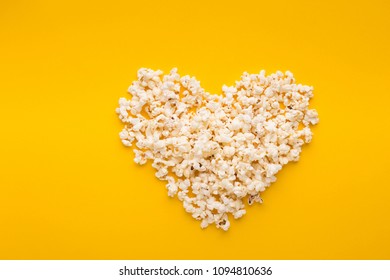 Love cinema concept. Popcorn arranged in heart shape on yellow background, top view, copy space