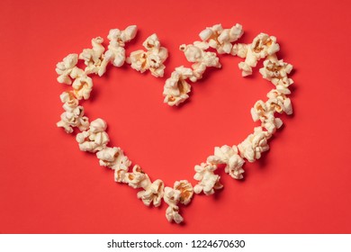 Love cinema concept of popcorn. Heart shaped white fluffy popcorn on red background with empty space for text