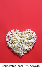 Love cinema concept of popcorn. Heart shaped white fluffy popcorn on red background with empty space for text. Valentine days concept.