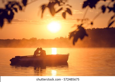 Liebe und Farben des romantischen goldenen Flusssonnenuntergangs mit Nebel und Silhouette eines Paares auf einem kleinen Boot, das durch Sonnenlicht beleuchtet wird