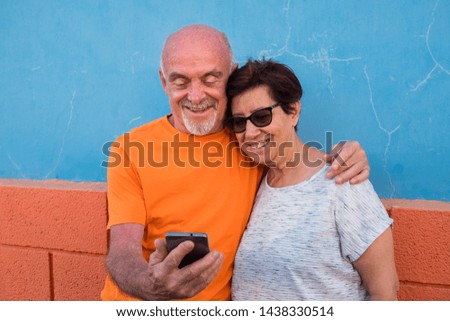 Love and complicity for a senior couple looking together at the same mobile phone. Smiles and relaxing moment. Orange and light blue color