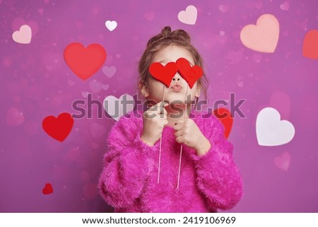 Love concept. Cheerful little girl in a bright fuchsia sweater happily posing with two red hearts on a pink background with hearts. Valentine's Day. Mothers Day. Birthday.