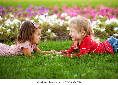 Love concept. Couple of kids, little boy and girl lying on the grass, holding hands and looking eye to eye. The tender feelings, ready for your text, logo or symbols. 