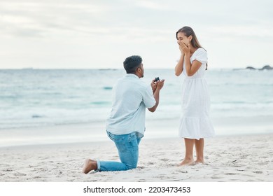 Love, couple and beach engagement proposal for marriage, partnership and commitment on ocean sea sand. Wow, shocked and surprised woman with romantic man on one knee presenting a union wedding ring
