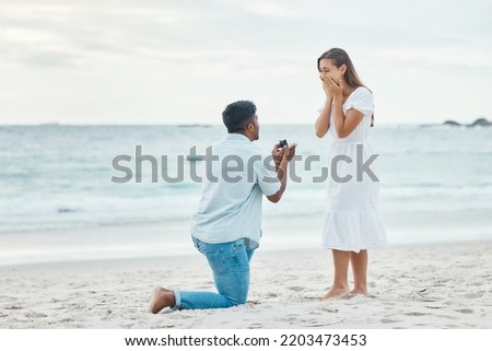 Love, couple and beach engagement proposal for marriage, partnership and commitment on ocean sea sand. Wow, shocked and surprised woman with romantic man on one knee presenting a union wedding ring