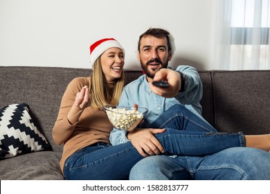 Love Couple With Christmas Hats Watching TV On Home Sofa