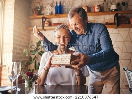 Love, couple elderly and gift to celebrate anniversary on date with smile, happy and excited together. Romance, mature man and older woman exchange present relax, being loving and bonding at home.