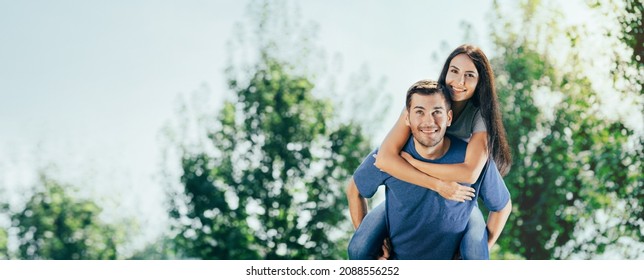 Love, dating, flirting, happy lovers, romantic concept - portrait of embracing excited smiling couple in piggy back pose, on nature. Man carrying his beautiful girl, wallking together outdoors. Wide.