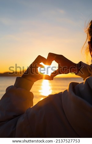 Love and freedon concept. Woman hands making heart shape over sunrise sky background