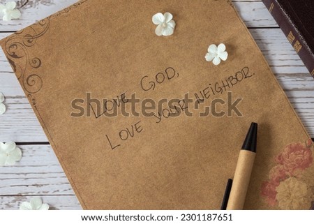 Love God, love your neighbor handwritten text verse on vintage paper with closed bible book and pen on wooden table. Christian faith and obedience to Jesus Christ, the greatest commandment concept.