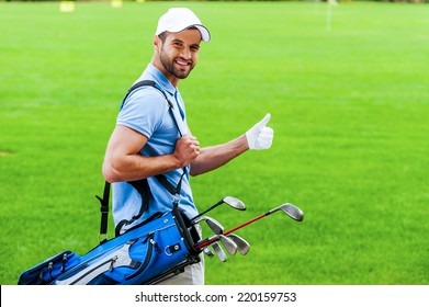 I love golfing! Rear view of young happy golfer carrying golf bag with drivers and looking over shoulder while standing on golf course