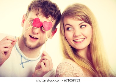 Love And Happiness Concept. Cheerful Enjoyable Young Couple With Little Small Hearts On Sticks Covering Woman Man Eyes. Lovers Blinded By Their Big Love.