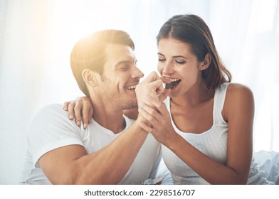 Love, happy couple eat chocolate in bedroom and care with smiling or laughing. Valentines day, married people sharing sweet snack and spending quality time in their home and romance or caring - Powered by Shutterstock