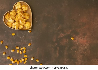 A love heart filled with popcorn shot against a dark metallic background with space for text, loose kernals, for National Popcorn Day 19 January 2021