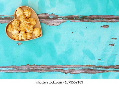 A love heart filled with popped corn kernals shot from above on a light blue wooden background with space for text for National Popcorn Day 19 January 2021. Some loose unpopped kernals loose on bg