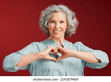 Love, heart and health retired woman with loving emoji sign, icon or symbol showing care or affection on red valentines day studio background. Grey, senior or pensioner with a trendy emoticon pose - Shutterstock ID 2191879409