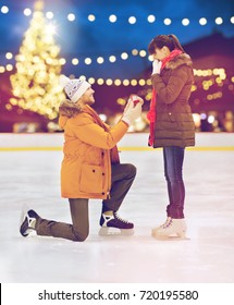 Love, Holidays And Relationships Concept - Happy Couple With Engagement Ring At Outdoor Skating Rink Over Christmas Lights Background