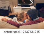 Love, kiss and couple watching tv on a sofa with romance, fun or bonding at home together. Television, movies or people embrace in a living room with trust, support or film, video or Netflix in house