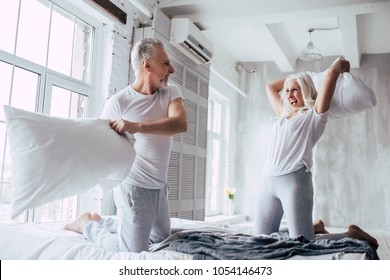 Love lives forever! Senior couple at home. Handsome old man and attractive old woman are enjoying spending time together. Having fun while having pillows battle. - Powered by Shutterstock