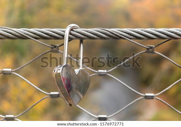 Love lock locked on the bridge. Silver colored\
padlock hanging on a wire\
rope