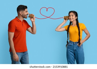 Love Message  Handsome Arab Guy Telling Romantic Words To His Girlfriend Through Tin Can Phone  Loving Middle Eastern Couple Making Drawn Red Heart With String  Standing Over Blue Background
