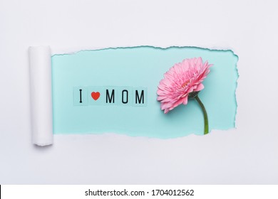 I love mom concept. Creative layout made of I love mom text and pink flower on blue background. Simple torn hole paper art.