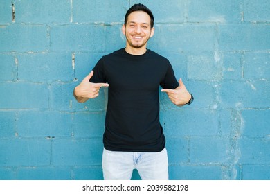 I Love My New Black T-shirt. Smiling Young Man Pointing To The Custom Print Design On His Chest 