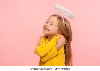 I love myself. Beautiful charming little girl with halo over head embracing herself and smiling from happiness, self-love concept, positive self-esteem. indoor studio shot isolated on pink background - Shutterstock ID 1694996083