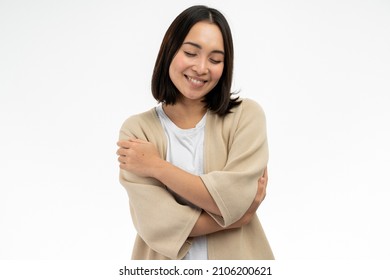I love myself. Portrait of pleased satisfied asian girl hugging herself and smiling, feeling comfortable and fulfilled, narcissistic egoistic person. Indoor studio shot white background  - Shutterstock ID 2106200621