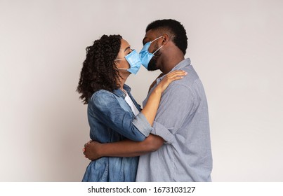Love On Quarantine. Romantic Black Couple Kissing Each Other In Protective Medical Masks On Face For Corona Virus Spread Prevention, Light Background