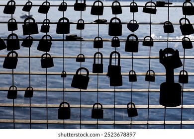 Love padlocks hanging on a metal grid bridge over a lake. Black lock shapes contrasting with water. Symbol of love and commitment. - Powered by Shutterstock