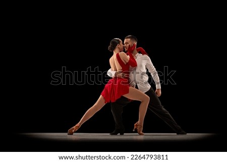 Love. Passionate attractive young man and woman, professional ballroom dancers dancing tango over black background. Concept of hobby, lifestyle, action, beauty of movements, emotions, fashion, art