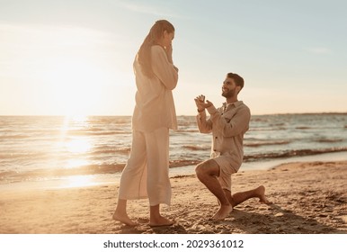 love and people concept - smiling young man with engagement ring making proposal to happy woman on beach - Powered by Shutterstock