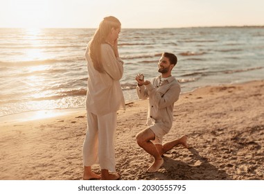 love and people concept - smiling young man with engagement ring making proposal to happy woman on beach - Powered by Shutterstock